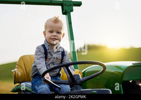 Growing up with good old fashioned farming values. Portrait of an adorable little boy riding a tractor on a farm. Stock Photo