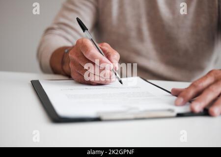 On the dotted line. Cropped shot of an unrecognizable businessman filling out a form on a clipboard while sitting at his desk in the office. Stock Photo