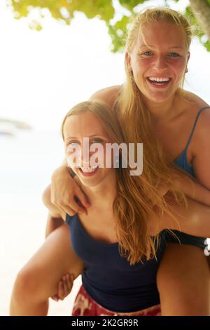 Piggybacks on the beach. Portrait of an attractive young woman piggybacking her friend on the beach. Stock Photo