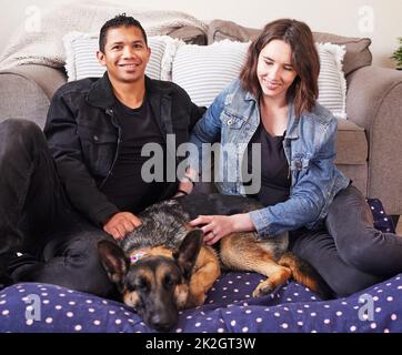 Our dog is like our baby. Shot of a young couple sitting in their living room with their German Shepherd during a day at home. Stock Photo