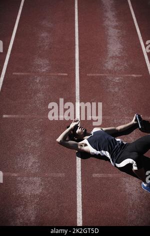 Life in the fast lane is tiring. A young runner lying down on the tartan track. Stock Photo