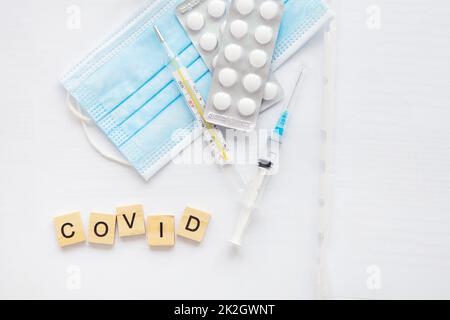 The inscription covid on a medical background, next to a thermometer, a syringe, pills, a protective mask. Medical theme. Concept: vaccination against coronavirus. Stock Photo