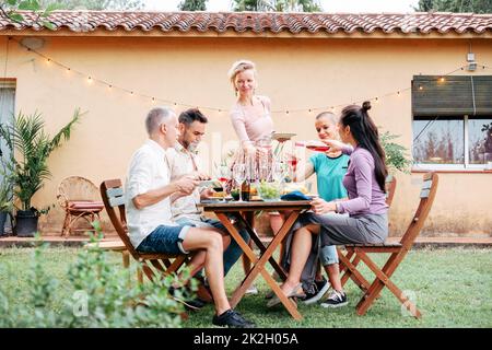 happy woman serving food to his friends enjoying dinner party celebration at sunset having fun reunion gathering in backyard at home. Lifestyle Stock Photo