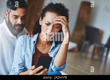 I accidentally sent that picture to your mother. Shot of a dismayed couple receiving bad news via a smartphone at home. Stock Photo