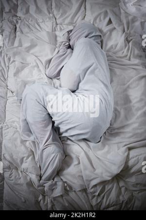 Mental health problems dont define who you are. Shot of a unrecognizable man laying under the covers in a mental asylum. Stock Photo