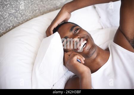 Connected with friends from the comfort of my bed. a handsome young man sitting in bed and using his cellphone. Stock Photo
