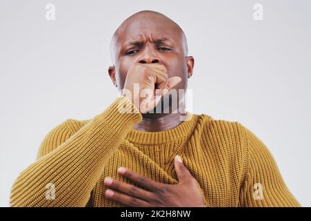 Flu season strikes again. Studio portrait of a handsome young man coughing against a grey background. Stock Photo