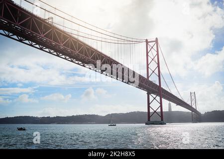 From one place to another. Low angle shot of a massive bridge over the ocean with clouds in the background outside during the day. Stock Photo