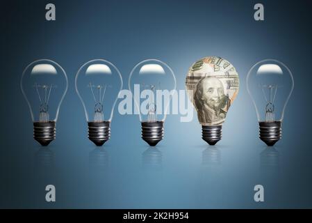 Five lightbulbs on a blue background and one of them wrapped with some 100 dollars banknotes Stock Photo