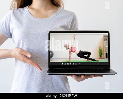 Virtual fitness class. Online training. Pilates tutorial. Woman hand recommending sport video program on laptop with athletic coach performing exercis Stock Photo