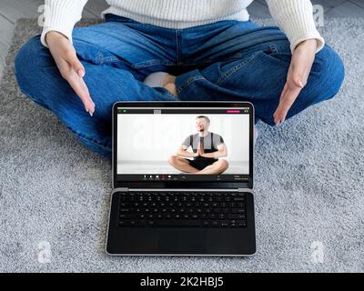 Online yoga class. Video chat. Virtual exercise. Web meditation program. Woman showing peaceful man sitting cross-legged with namaste position on lapt Stock Photo
