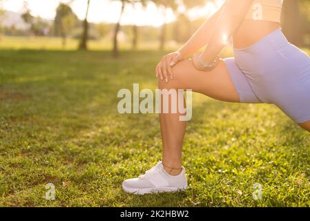 Close up shot of A woman with a blue tights stretching legs and warming up in a public park in the morning. Stock Photo