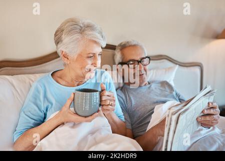 We still like the good old fashioned newspaper. Cropped shot of a senior man reading a newspaper in bed while his wife drinks a cup of coffee. Stock Photo