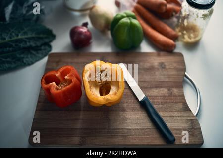 Essential ingredients. High angle shot of chopped peppers on a cutting board surround by various vegetables on a kitchen counter. Stock Photo