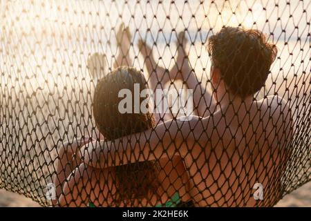 Chilling at the beach. Rear view shot of a young couple relaxing on a hammock at the beach. Stock Photo