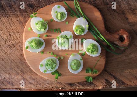 Stuffed deviled eggs appetizer with avocado and leek on cutting board. Top view Stock Photo
