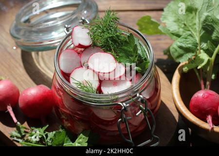 Red radish pickled glass jar on a wooden table. Fermented veggies preserves. Stock Photo