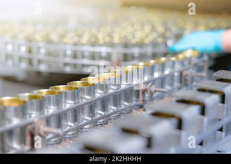 Canned fish factory. Food industry. Canned food factory. Sardines in tin cans. Food processing production line. Food manufacturing industry. Many can on a conveyor belt and blurred worker hand. Stock Photo