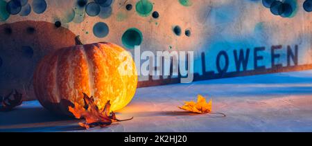 Halloween holiday pumpkin on concrete stone floor with autumn leaves and dark dirty spooky bokeh Stock Photo