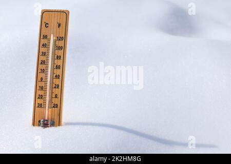 Wooden thermometer standing in the snow, sun casting curvy shadow, red column showing 0 degrees Celsius temperature. Winter / snow coming concept. Stock Photo