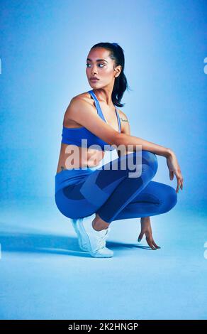 She's in full workout mood. Full length shot of an attractive young sportswoman posing in studio against a blue background. Stock Photo