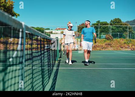 Let the games begin. Full length shot of two young tennis players talking while walking together outdoors on a tennis court. Stock Photo
