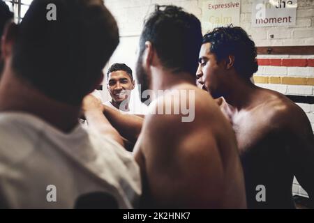 Team spirit is everything. Cropped shot of a group of handsome young rugby players standing together in a huddle in a locker room. Stock Photo