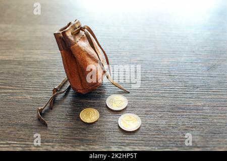Vintage leather pouch on wooden desk, with euro coins next to it Stock Photo