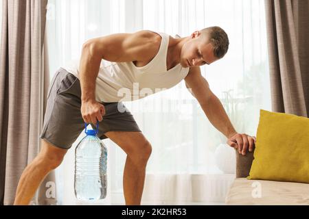 Young athletic man using big bottle of water for home workout Stock Photo