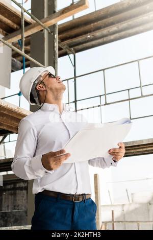 Man architect or businessman wearing hard hat and holding blueprints on a  construction site Stock Photo - Alamy