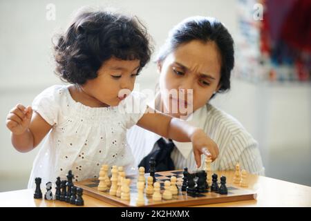 When did she get this smart. A cute little girl playing chess while her mom looks on. Stock Photo