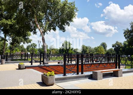 Rest area with bench and staircase surrounded by blooming flowers and ornamental shrubs. Place to rest in the city park Stock Photo