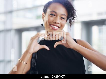 I love business. Cropped shot of a young businesswoman showing a heart sign while walking through a modern office. Stock Photo