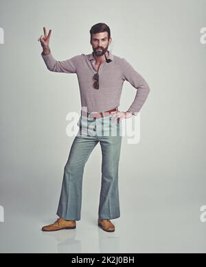 Peace out. Studio shot of a handsome man striking a pose while wearing retro 70s style clothing. Stock Photo