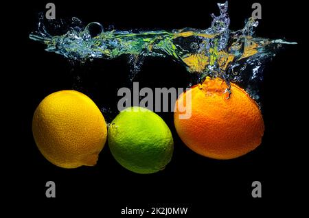 Lemon, kiwi and orange dropped in water with splashes isolated on black background. Stock Photo