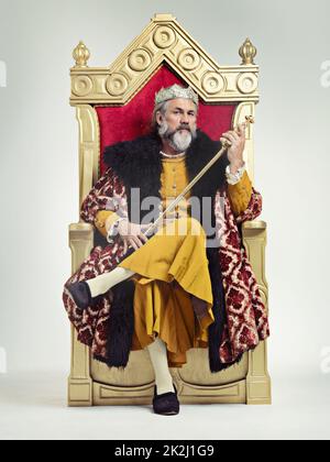 Throne of the kings. Studio shot of a richly garbed king sitting on a throne holding his scepter. Stock Photo