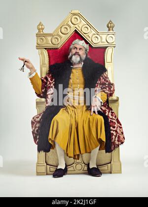 Servants Come hither. Studio shot of a richly garbed king sitting on a throne. Stock Photo