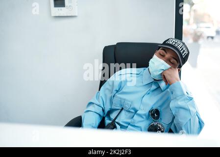 When fighting crime turns into fighting fatigue. Shot of a masked young security guard sleeping at a desk in an office. Stock Photo