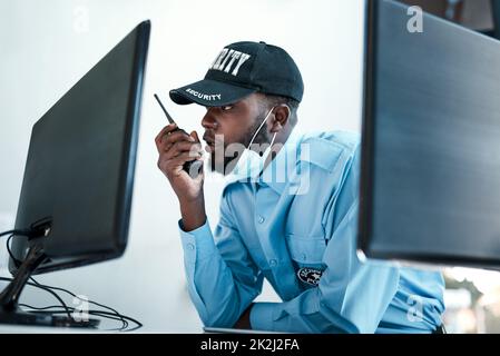 Your direct connection to first rate protection. Shot of a young security guard using a two way radio while monitoring the cctv cameras. Stock Photo