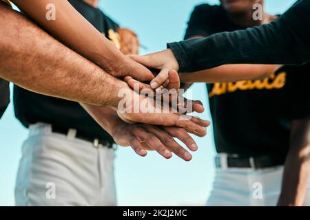 They all work together for a single purpose. Shot of a team of young baseball players joining their hands together in a huddle during a game. Stock Photo