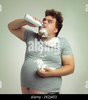 My diet said I need to eat light foods. Shot of an overweight man filling his mouth with whipped cream. Stock Photo