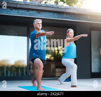 Perfect coordination. Full length shot of a mature and happy couple doing yoga exercise outside of their home. Stock Photo