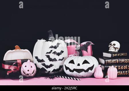 Pink and white Halloween decor with black and white pumpkins, spell books and spiders on black background with copy space Stock Photo