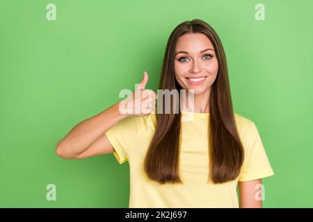 Photo of sweet optimistic satisfied girl with straight hairdo wear yellow t-shirt showing thumb up isolated on green color background Stock Photo