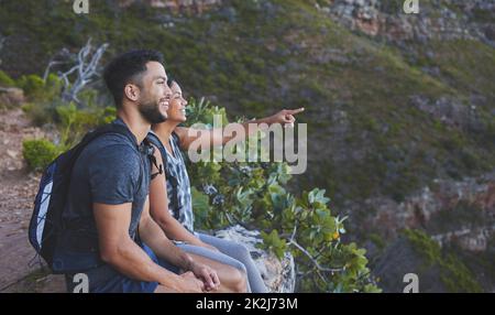 Look at how amazing that view is. Shot of a young couple enjoying the sunset view while out on a hike on a mountain range. Stock Photo