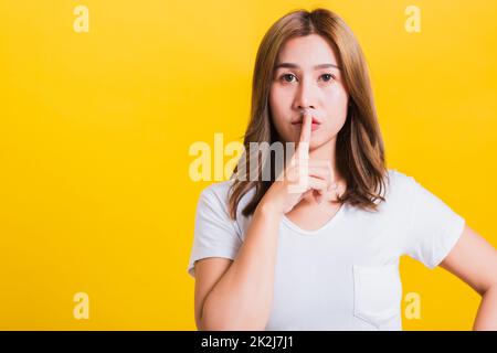 woman teen smile standing wear t-shirt making finger on lips silent quiet gesture Stock Photo