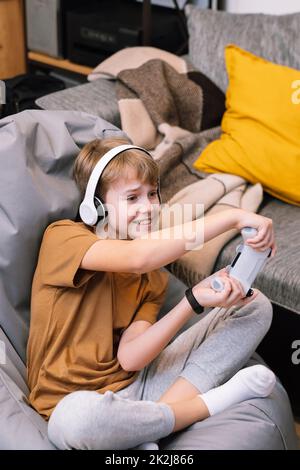 Teen boy actively and recklessly playing video game with joystick sitting on frameless beanbag chair Stock Photo