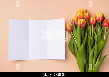 Mockup of trifold brochure on a beige background with a bouquet of tulips. Stock Photo
