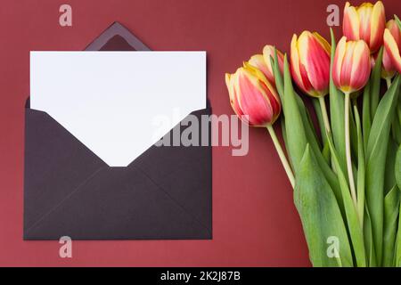 White Horizontal Card mockup or thank you card template in an envelope with bouquet of tulips on burgundy background. Stock Photo