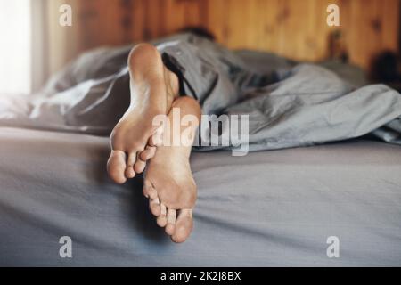 Toot tired to shower before bed. Closeup shot of a mans dirty feet while hes sleeping in bed. Stock Photo